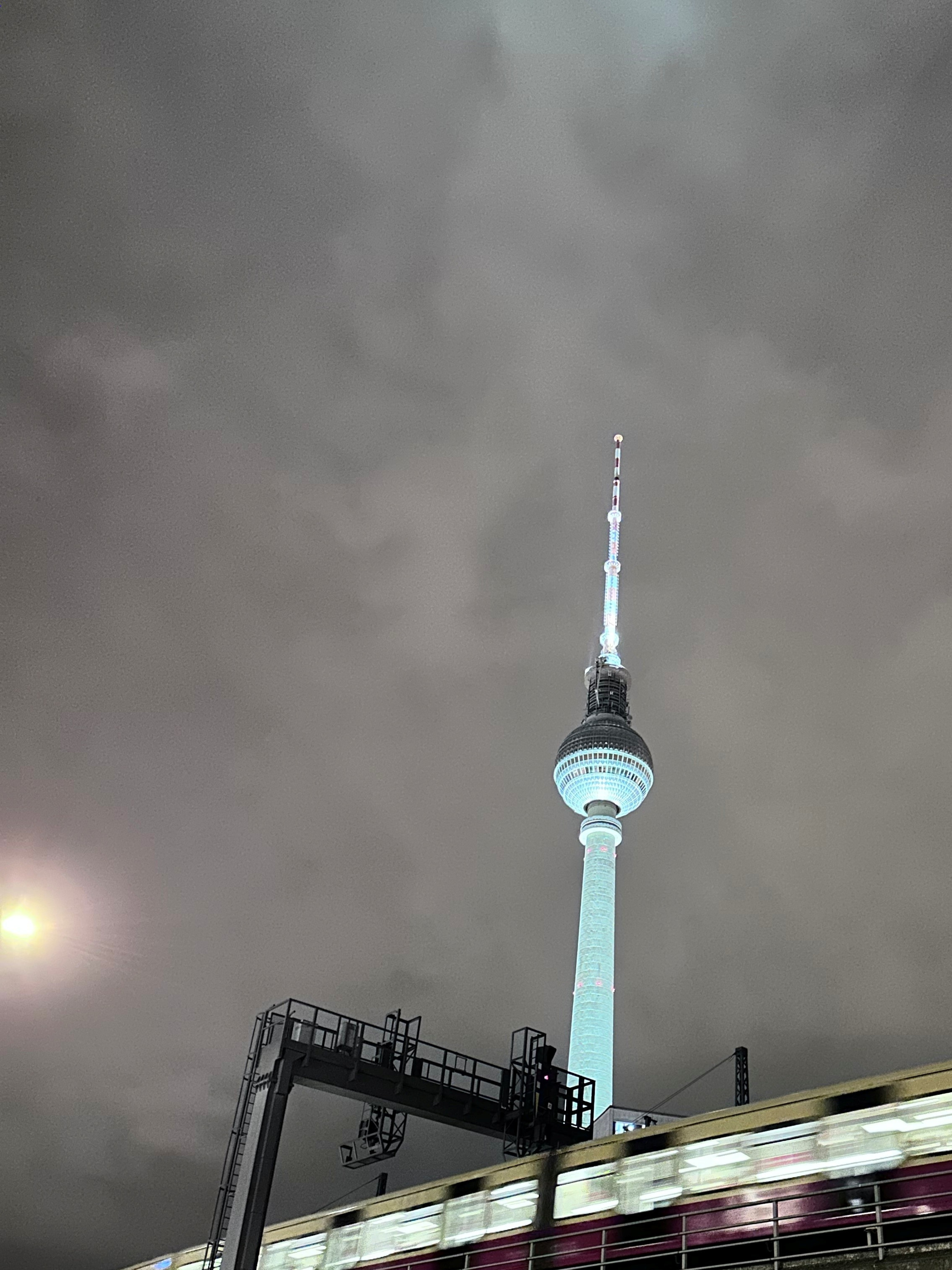Berliner Fernsehturm und vorbeifahrende Bahn bei Nacht